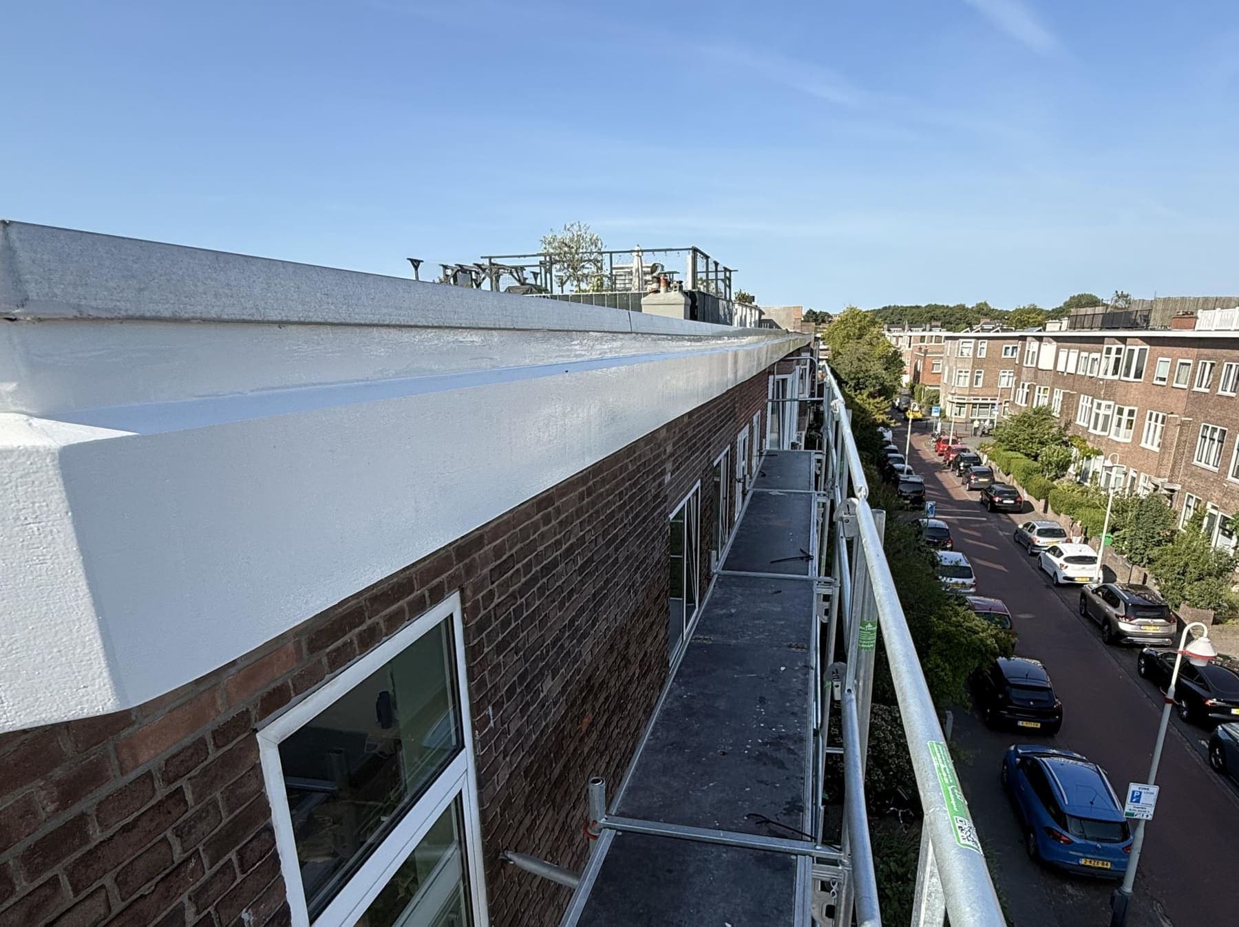 Vers wit gelakte boeidelen langs de dakrand van een woonblok, met uitzicht over de straat.