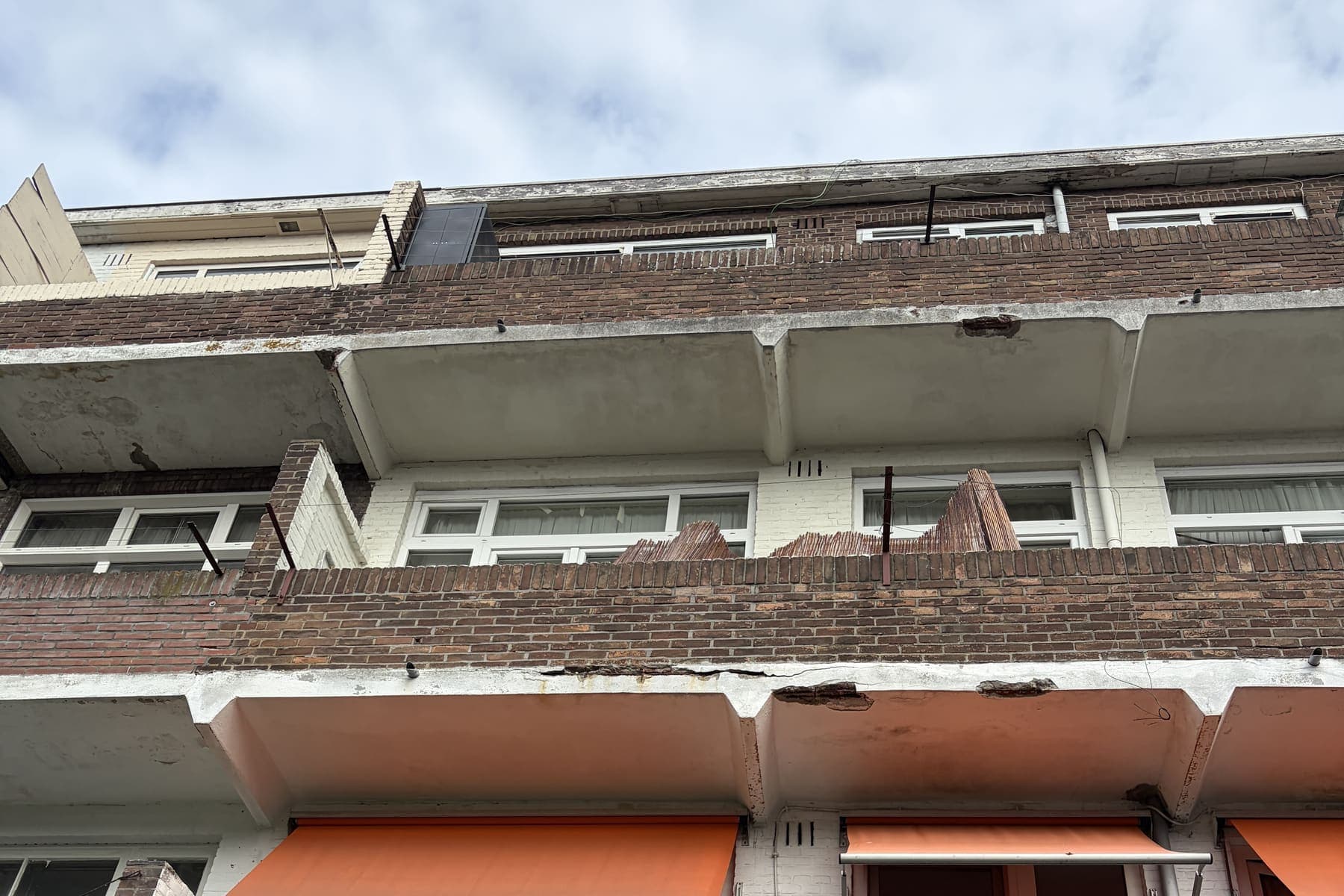 Balkons van een portiekflat met afgebrokkeld beton en zichtbare betonrot langs de balkonranden.